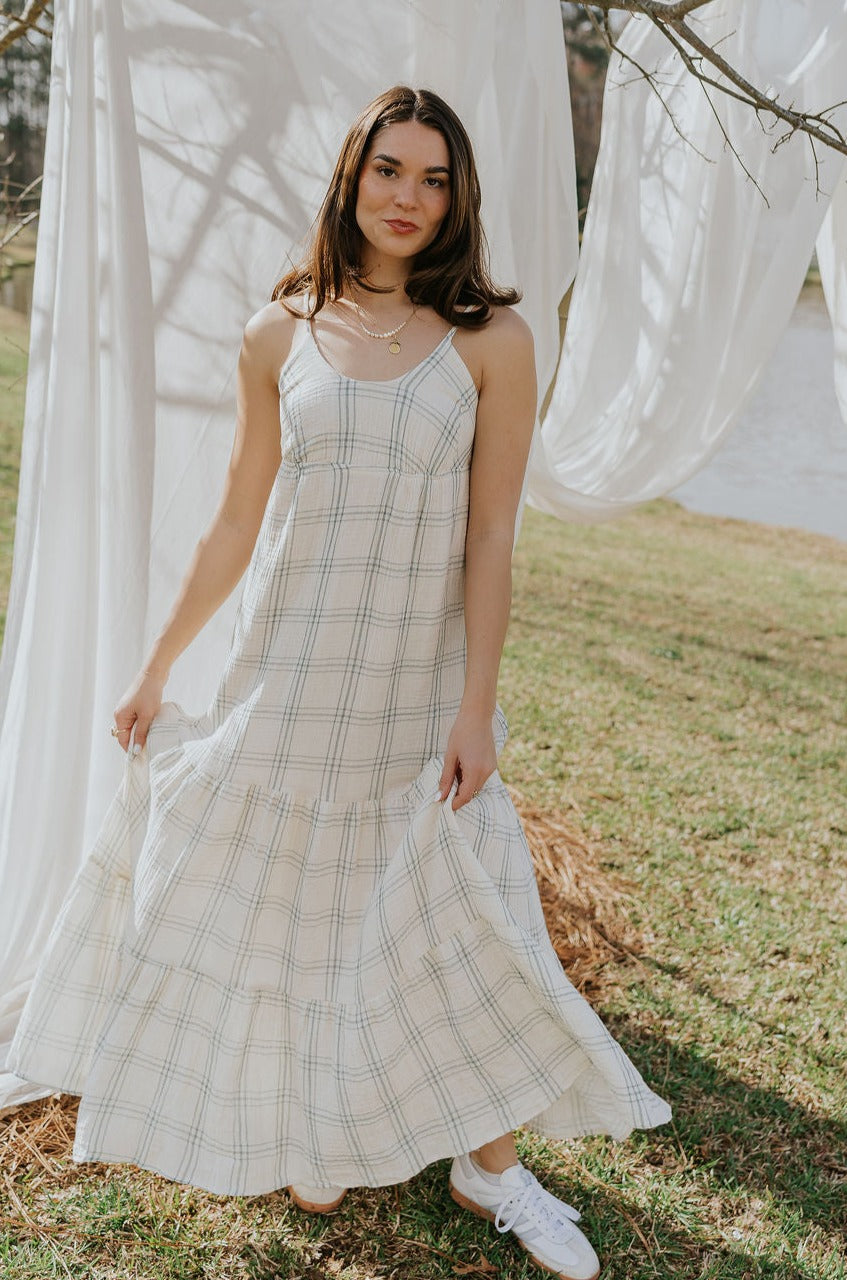 Full body front view of female model wearing the Milana Ivory & Blue Plaid Maxi Dress that has ivory fabric with blue plaid, spaghetti straps, tiered skirt, and ties in the back.