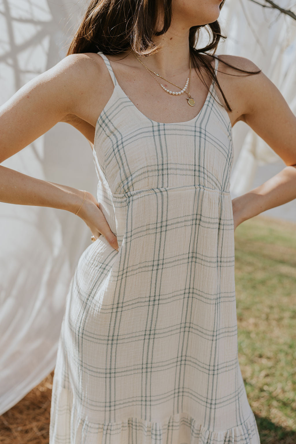 Close upper body front view of female model wearing the Milana Ivory & Blue Plaid Maxi Dress that has ivory fabric with blue plaid, spaghetti straps, tiered skirt, and ties in the back.
