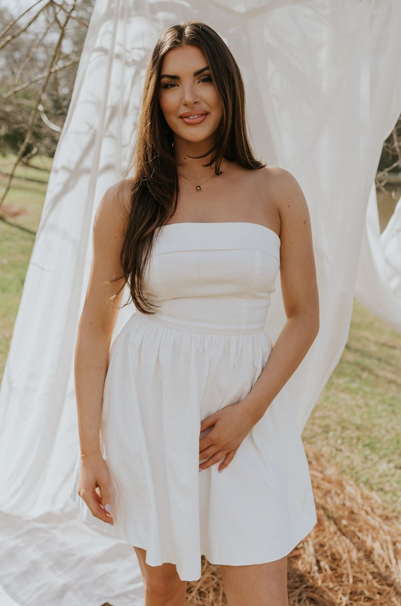Front view of female model wearing the Abigail Strapless Flare Mini Dress in white which features features Mini Length, Lining, Two Side Pockets, Strapless and Monochrome Back Zipper with Hook Closure.