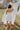Full body back view of female model wearing the Abigail Strapless Flare Mini Dress in white which features features Mini Length, Lining, Two Side Pockets, Strapless and Monochrome Back Zipper with Hook Closure.
