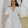 Front view of female model wearing the Madeline White Eyelet Romper that has white fabric with eyelet details, short puff sleeves, a vneck, and a keyhole back with a tie.