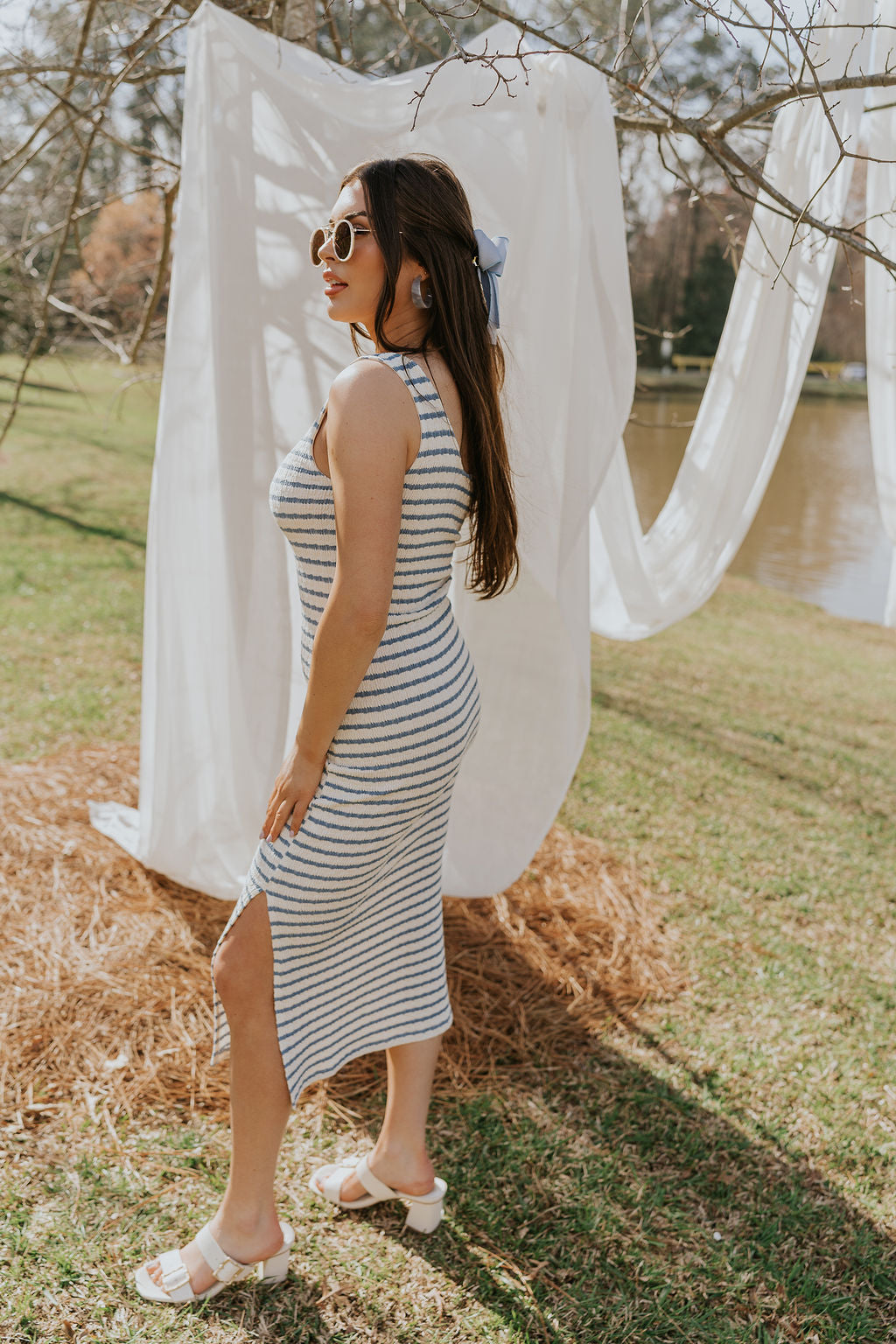 Full body side view of female model wearing the Casey Cream & Blue Striped Midi Dress that has cream and blue horizontal stripes, bodycon fit, thick straps, a side slit, and round neck.