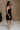 Full body side view of female model wearing the Abigail Strapless Flare Mini Dress in black which features features Mini Length, Lining, Two Side Pockets, Strapless and Monochrome Back Zipper with Hook Closure.