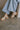 Left side view of female model wearing the Dasha Sandal in Off White which features off white upper leather fabric, kork platform sole, block heel, criss-cross strap and gold adjustable buckle closure