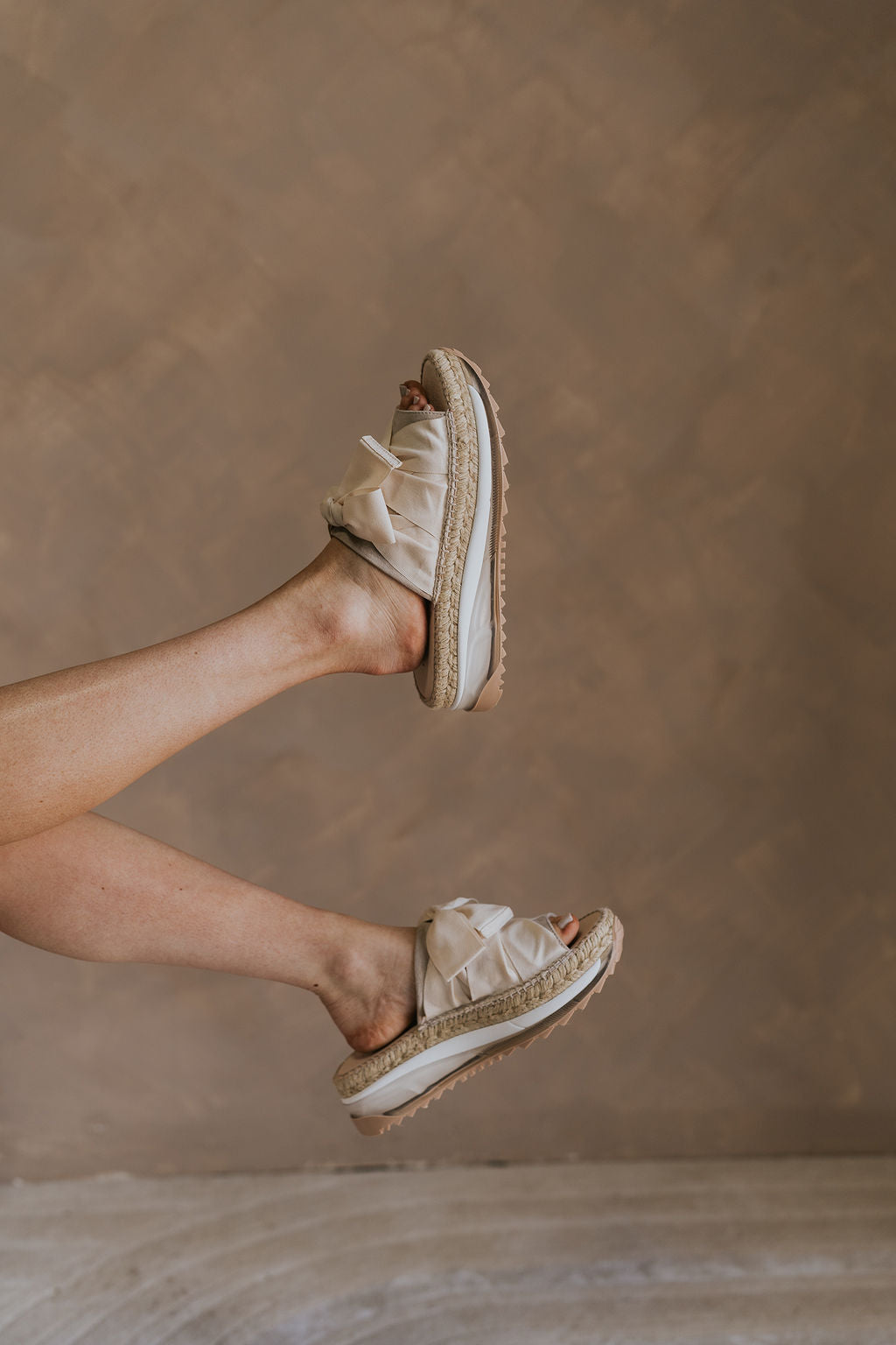 Side view of female model wearing the Chapmin Sport Sandal which features slip-on style, slingback design, round open toe, natural suede toe strap, triple-stacked platform sole, espadrille detailing, clear midsole, tread outsole, oversized ribbon laces, self-tie slingback strap