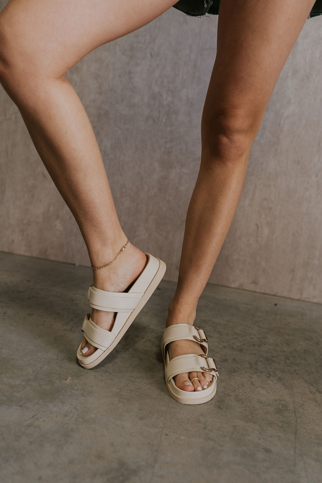 Front view of female model wearing the Soya Sandal in White Leather which features white leather fabric, chunky sole, gold hammered metallic ring accents and slip-on style
