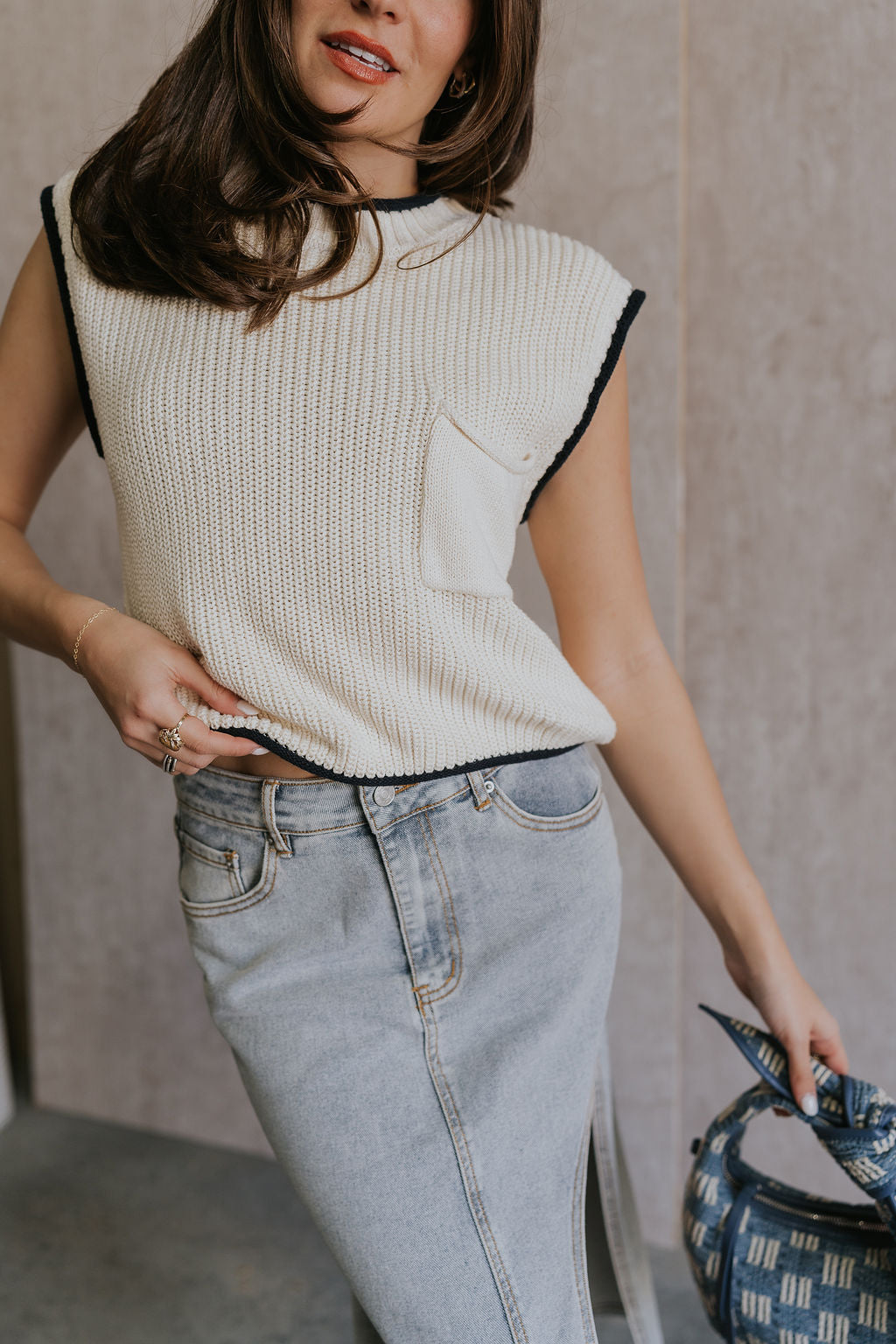 Close up view of female model wearing the Vivian Ivory & Navy Knit Sleeveless Sweater which features Cream Cable Knit Fabric, Navy Trim Details, Left Front Chest Pocket, High Neckline and Sleeveless.