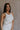 Frontal side view of female model wearing the Sienna Off White & Tan Sleeveless Tank which features White Ribbed Fabric, Tan Trim Details, Round Neckline and Sleeveless