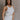 Side view of female model wearing the Sienna Off White & Tan Sleeveless Tank which features White Ribbed Fabric, Tan Trim Details, Round Neckline and Sleeveless