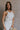 Side view of female model wearing the Sienna Off White & Tan Sleeveless Tank which features White Ribbed Fabric, Tan Trim Details, Round Neckline and Sleeveless
