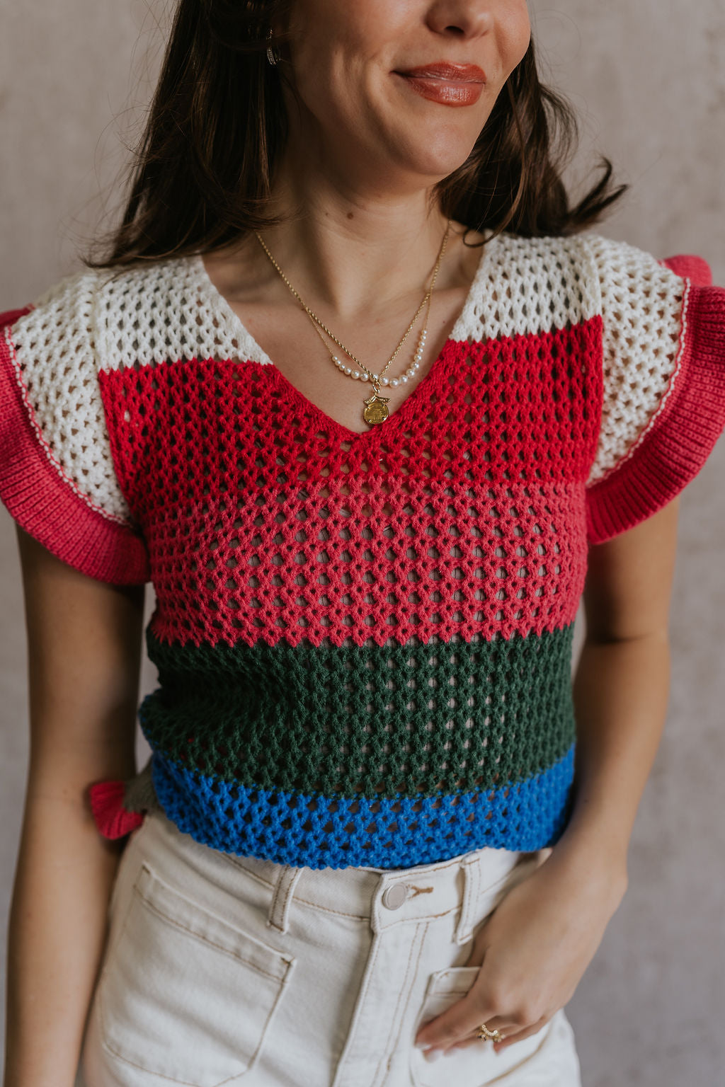 Close up view of female model wearing the Andrea Pink Multi Knit Ruffle Top which features Blue, Green, Pink, Grey and Cream Open Knit Fabric, Ruffle Hem, V-Neckline and Short Sleeves