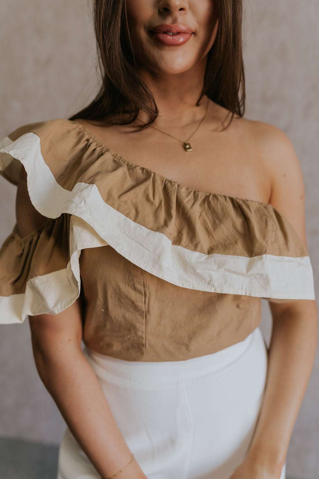 Close up view of female model wearing the Rosalie Khaki & Cream Ruffle One-Shoulder Top which features Brown and Cream Lightweight Fabric, Cropped Waist, Side Zipper with Hook Closure, One-Shoulder Ruffle Strap and Sleeveless