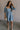 Full body view of female model wearing the Hallie Light Chambray Mini Dress which features Light Chambray Tencel Fabric, Mini Length, Square Neckline, Half Sleeves with Ruffle Hem Details and  Smocked Back