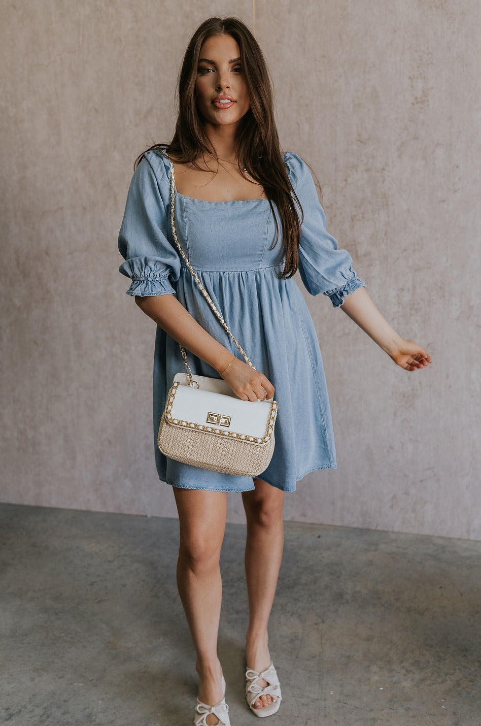 Full body view of female model wearing the Hallie Light Chambray Mini Dress which features Light Chambray Tencel Fabric, Mini Length, Square Neckline, Half Sleeves with Ruffle Hem Details and Smocked Back