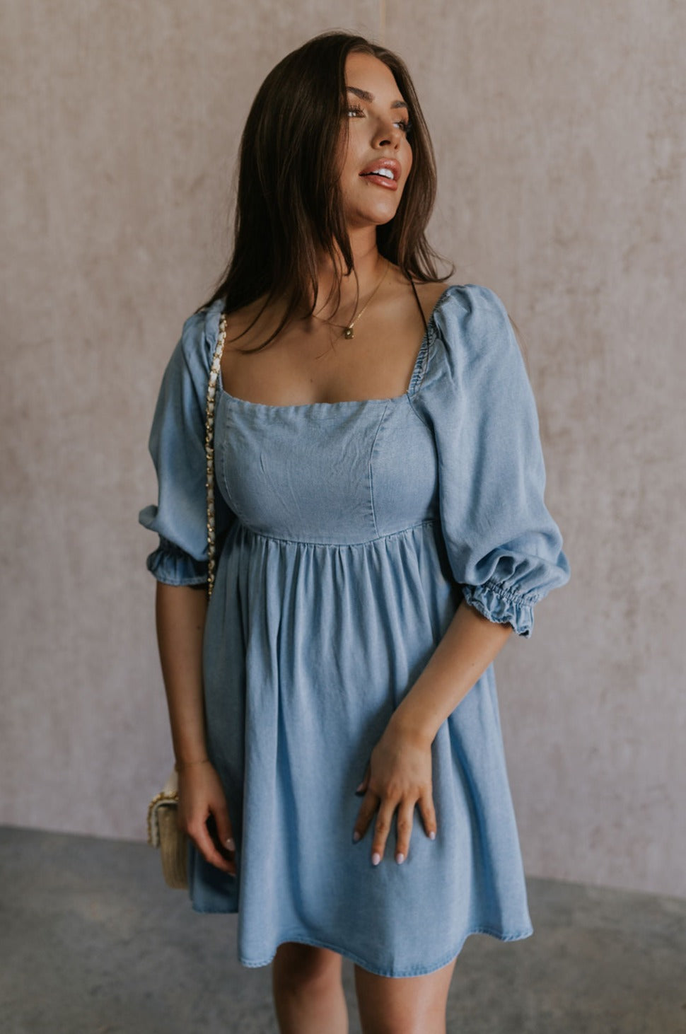 Front view of female model wearing the Hallie Light Chambray Mini Dress which features Light Chambray Tencel Fabric, Mini Length, Square Neckline, Half Sleeves with Ruffle Hem Details and Smocked Back
