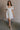 Full body view of female model wearing the Julia Off White Short Puff Sleeve Mini Dress which features Off White Stripe Sheer Fabric, White Lining, Mini Length, Ruched Upper, Sweetheart Neckline, Short Puff Sleeves and Back Cut-Out Detail with Zipper and Tie Closure