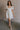 Full body view of female model wearing the Julia Off White Short Puff Sleeve Mini Dress which features Off White Stripe Sheer Fabric, White Lining, Mini Length, Ruched Upper, Sweetheart Neckline, Short Puff Sleeves and Back Cut-Out Detail with Zipper and Tie Closure