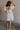 Full body back view of female model wearing the Julia Off White Short Puff Sleeve Mini Dress which features Off White Stripe Sheer Fabric, White Lining, Mini Length, Ruched Upper, Sweetheart Neckline, Short Puff Sleeves and Back Cut-Out Detail with Zipper and Tie Closure