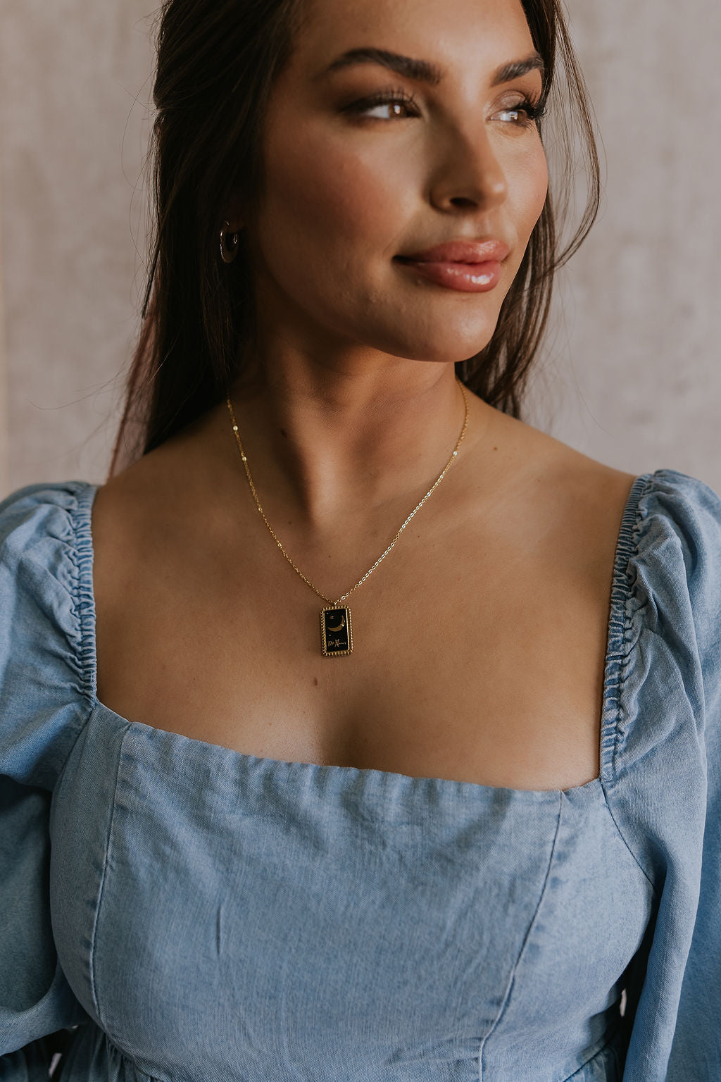 Close up view of female model wearing the Naomi Black & Gold Crescent Necklace which features adjustable gold chain layer with a gold and black rectangle medallion, gold crescent moon detail 
