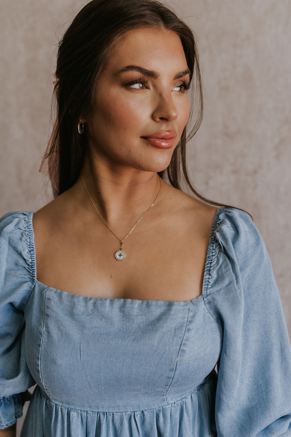 Front view of female model wearing the Angelica White & Gold Star Medallion Necklace which features adjustable gold chain layer with an ivory circle medallion, gold star design and rhinestones around the medallion