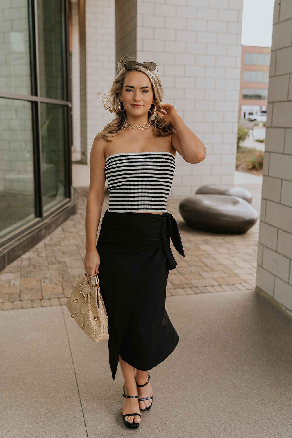 Full body front view of female model wearing the Londyn White & Black Striped Tube Top that has horizontal white and black stripes and a straight strapless neckline. Worn with black skirt.