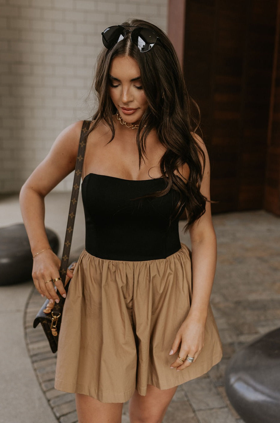 Front view of female model wearing the Parker Black & Mocha Strapless Romper that has a black upper with a strapless neck attached to mocha shorts with a wide fit and pockets.