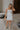 Full body view of female model wearing the Emerson White Blue Floral Ruffle Mini Dress which features White Lightweight Fabric, Blue Floral Print, Ruffle Hem Design, Square Neckline and sleeveless