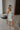 Full body side view of female model wearing the Emerson White Blue Floral Ruffle Mini Dress which features White Lightweight Fabric, Blue Floral Print, Ruffle Hem Design, Square Neckline and sleeveless