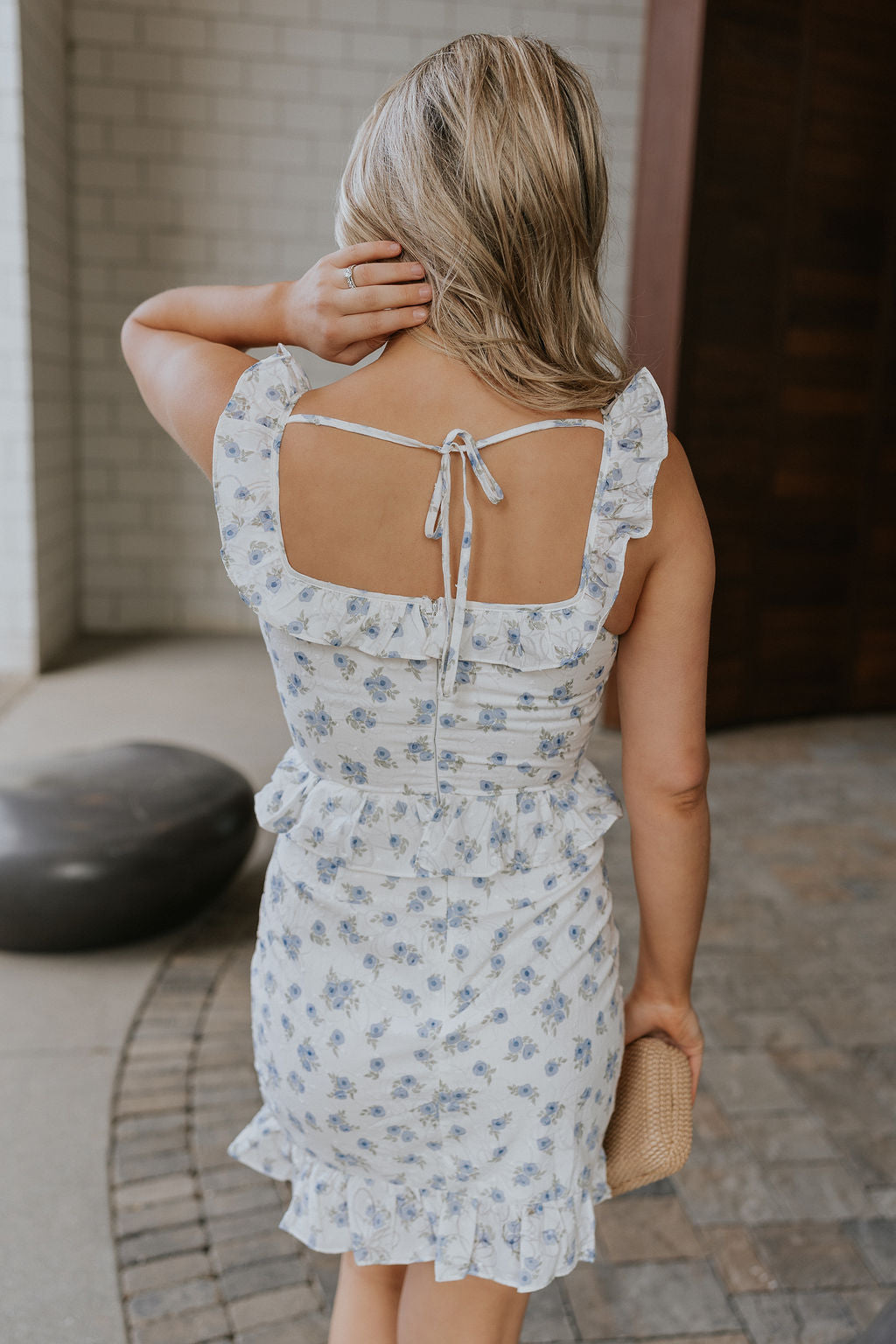 Back view of female model wearing the Emerson White Blue Floral Ruffle Mini Dress which features White Lightweight Fabric, Blue Floral Print, Ruffle Hem Design, Square Neckline and sleeveless