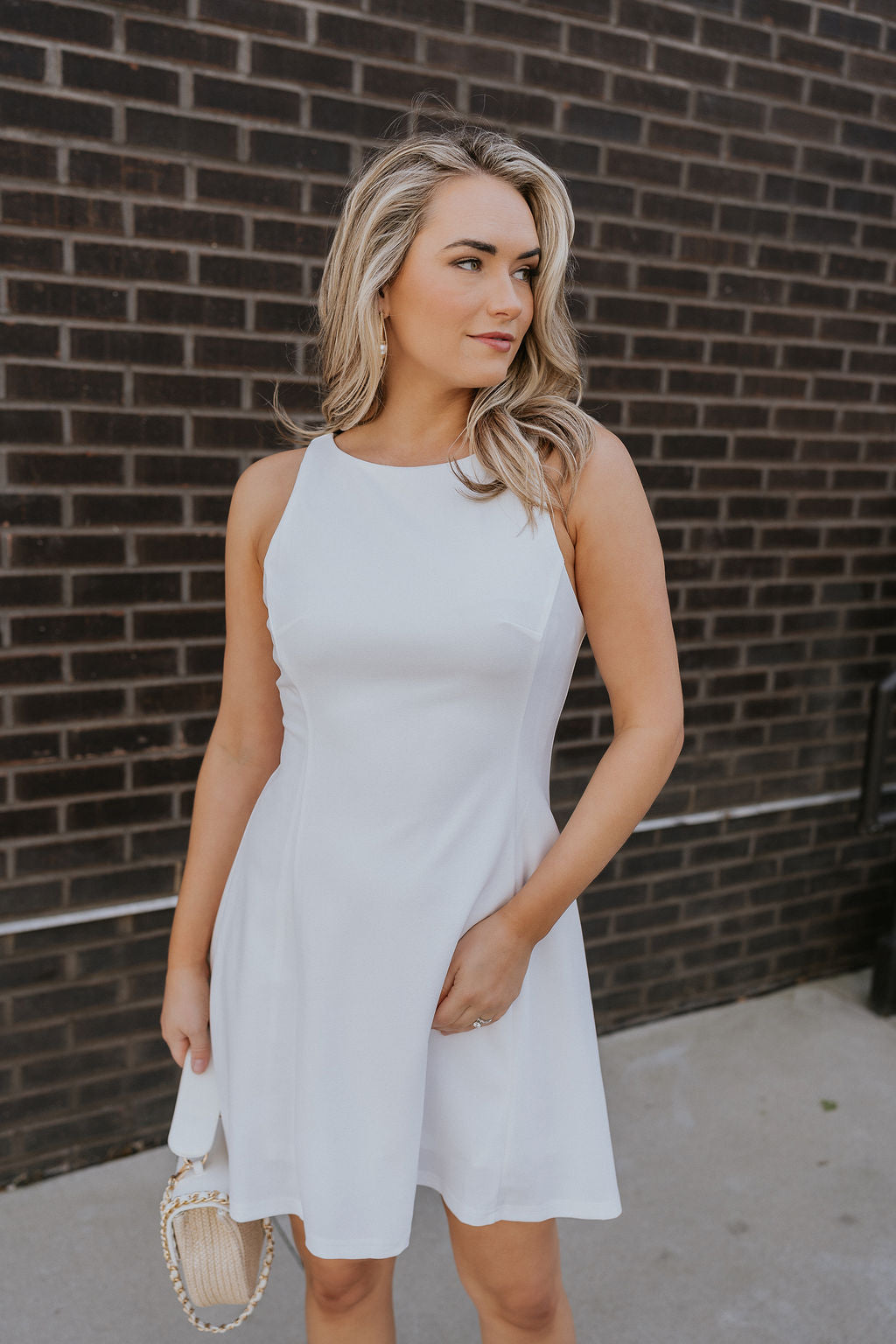 Front view of female model wearing the Catherine White Sleeveless Mini Dress that has a high round neck, sleeveless body, and flared mini silouette.