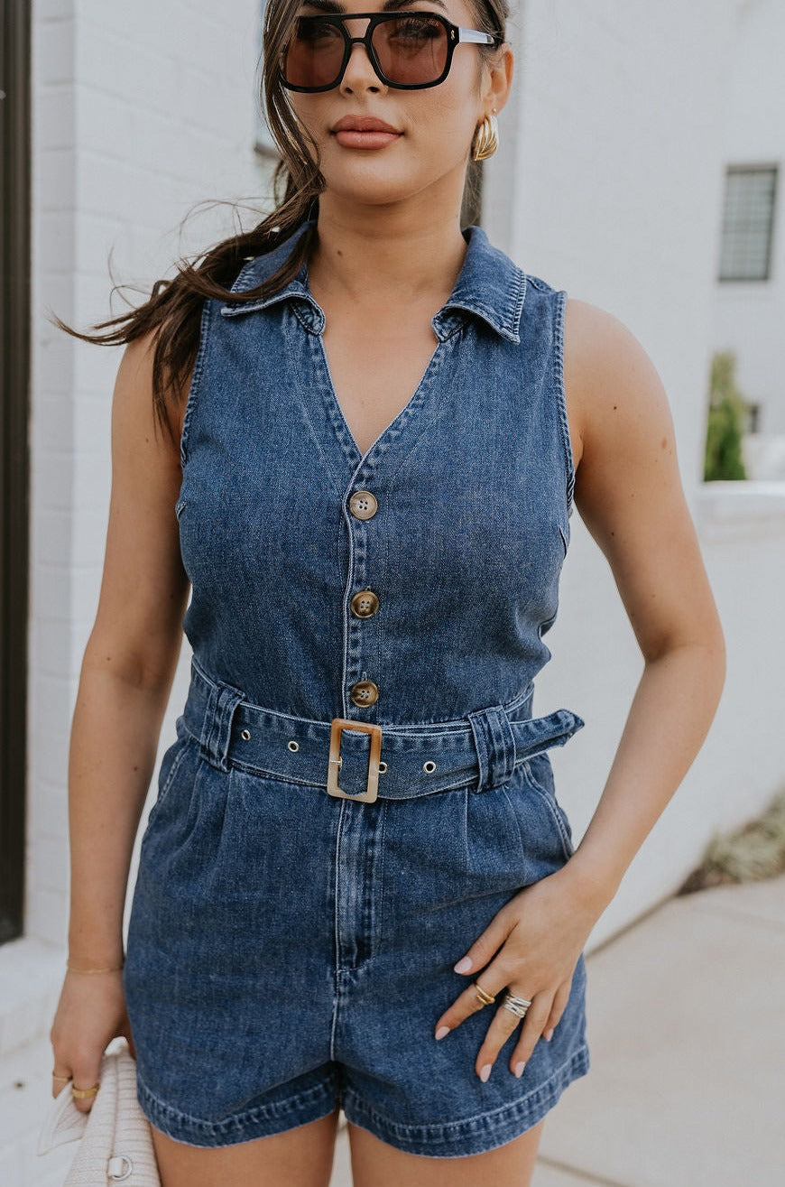 Front view of female model wearing the Georgia Belted Denim Romper in medium wash, that has a button up front, collar, and belted waist. 
