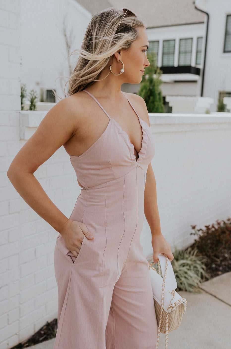 Side view of female model wearing the Aleah Mauve Pink Sleeveless Jumpsuit which features Mauve Pink Lightweight Fabric, Wide Leg Pants, Upper Ruched Detail, Two Side Pockets, Scooped Neckline, Adjustable Straps and Open Back with Tie Closure and Zipper