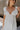 CLose up view of female model wearing the Rhea White Floral Ruffle Mini Dress which features Off White Lightweight Fabric, Mini Babydoll Style, Off White Lining, Monochrome Floral Print with Silver Metallic Thread, Sweetheart Neckline, Ruffle Straps and Open Back with Tie Closure