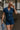 Front view of female model wearing the Mavis Denim Short Sleeve Zip-Up Romper which features Denim Fabric, Two Front Pockets, Front Zipper Closure, Adjustable Monochrome Belt with Loops, Collared Neckline and Short Sleeves