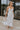 Full body view of female model wearing the Morgan Off White Eyelet Maxi Dress which features White Lightweight Fabric, Eyelet Pattern, White Lining, Maxi Length, Tiered Body, Sweetheart Neckline, Adjustable Straps and Open Back with Bow Tie 