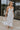 Full body view of female model wearing the Morgan Off White Eyelet Maxi Dress which features White Lightweight Fabric, Eyelet Pattern, White Lining, Maxi Length, Tiered Body, Sweetheart Neckline, Adjustable Straps and Open Back with Bow Tie 