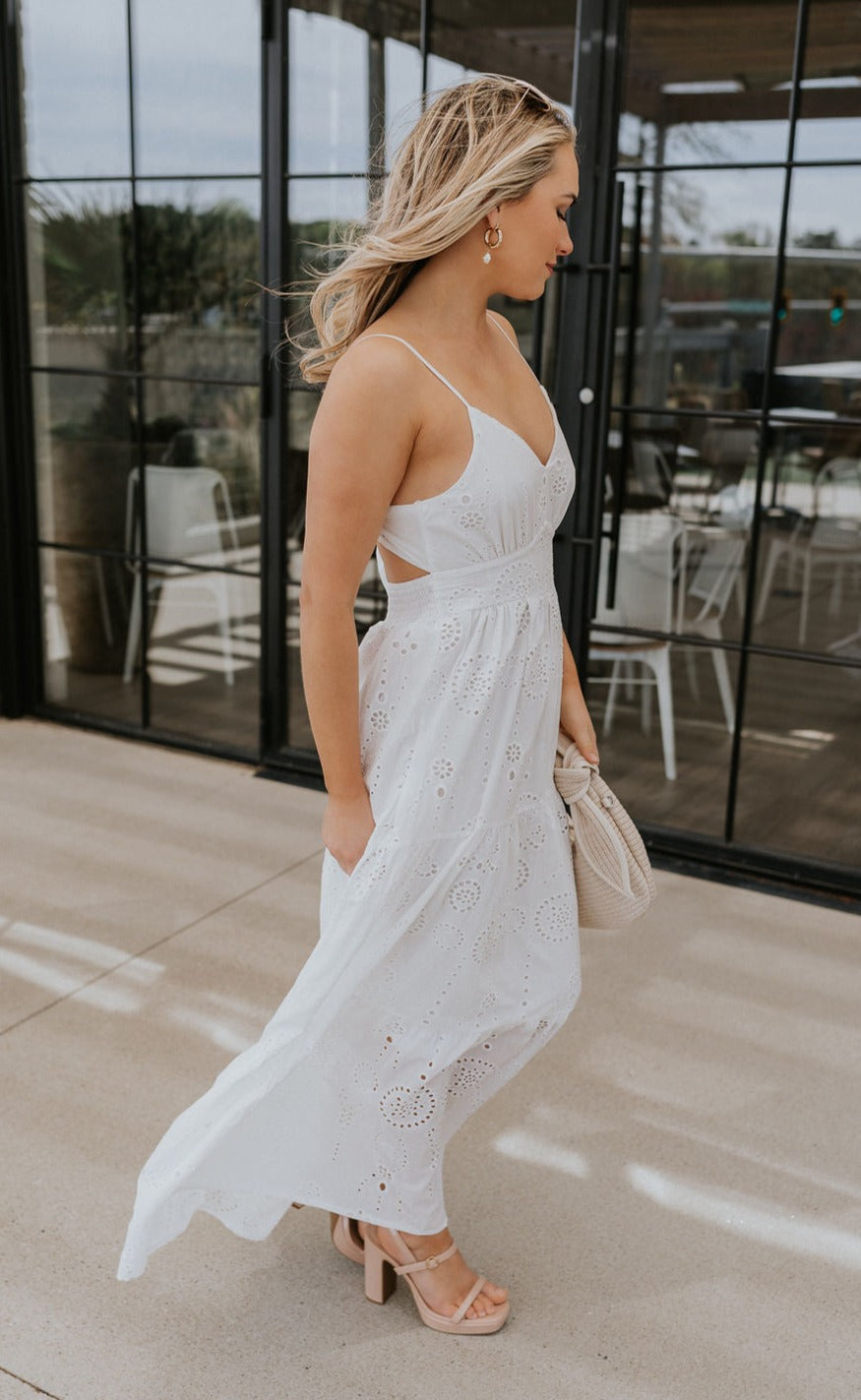 Full body side view of female model wearing the Morgan Off White Eyelet Maxi Dress which features White Lightweight Fabric, Eyelet Pattern, White Lining, Maxi Length, Tiered Body, Sweetheart Neckline, Adjustable Straps and Open Back with Bow Tie