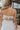 Back view of female model wearing the Morgan Off White Eyelet Maxi Dress which features White Lightweight Fabric, Eyelet Pattern, White Lining, Maxi Length, Tiered Body, Sweetheart Neckline, Adjustable Straps and Open Back with Bow Tie