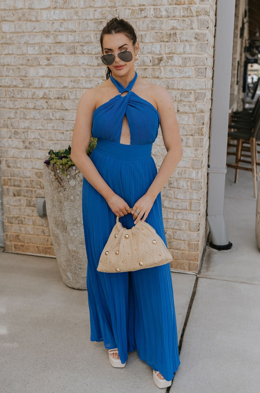 Full body view of female model wearing the Juliette Blue Halter Tie Pleated Jumpsuit which features  Blue Lightweight Fabric, Pleated Wide Pant Legs, Front Key Hole Design, Halter Neckline Tie Closure and  Open Back