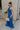 Full body side view of female model wearing the Juliette Blue Halter Tie Pleated Jumpsuit which features Blue Lightweight Fabric, Pleated Wide Pant Legs, Front Key Hole Design, Halter Neckline Tie Closure and Open Back