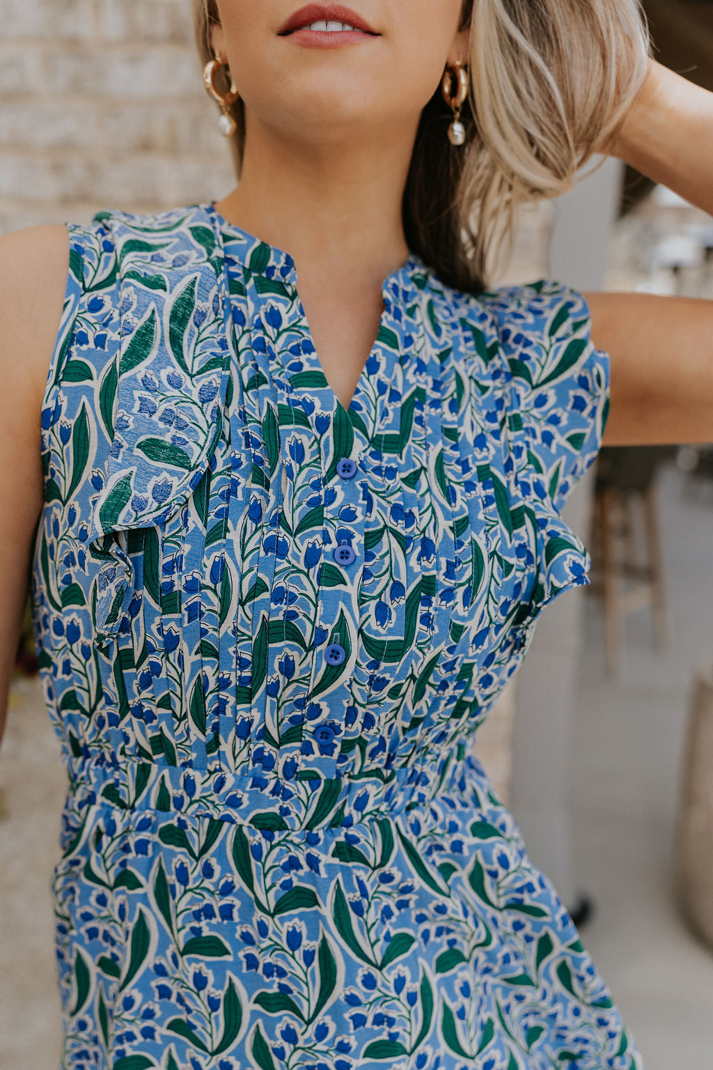  Close up view of female model wearing the June Blue & Green Floral Ruffle Mini Dress which features Blue and Green Floral Print, Ruffle Tiered Design, Mini Length, High Neck with V-Cutout and Sleeveless