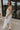 Side viiew of female model wearing the Lina Off White Halter Neckline Maxi Dress which features White Lightweight Fabric, White Lining, Maxi Length, Slit Detail, Halter Tie Neckline with Key Hole Detail and Elastic Back