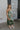 Full body side view of female model wearing the Azalea Dark Sage Satin Ruffle Midi Dress which features Green satin fabric Diagonal ruffles down the bust and waist, Spaghetti straps, V-Neckline, Elastic across the back top and Midi length
