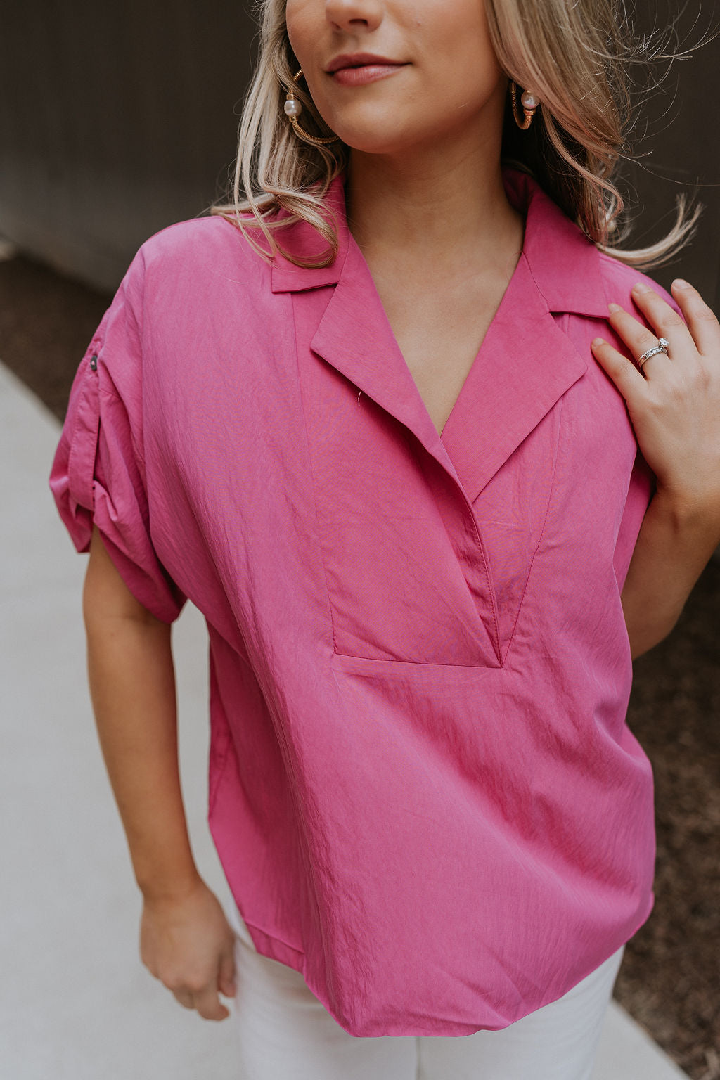 Close up view of female model wearing the Everlee Pink Short Sleeve Top which features Pink Lightweight Fabric, Short Sleeves with Pearlescent Buttoned Cuffs and Collar Neckline with V-Cutout
