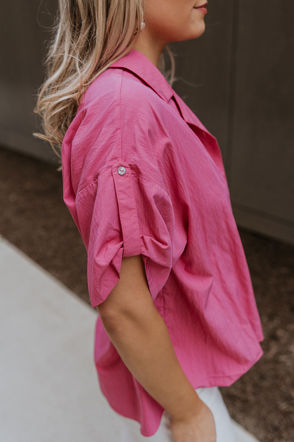 Side view of female model wearing the Everlee Pink Short Sleeve Top which features Pink Lightweight Fabric, Short Sleeves with Pearlescent Buttoned Cuffs and Collar Neckline with V-Cutout