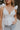 Close up view of female model wearing the Lauren White Ruffle Plunge Neckline Tank which features White Lightweight Fabric, Peplum Hem Body, Sweetheart Neckline, Ruffle Straps, Open Back Corset Tie and Back Zipper with Hook Closure
