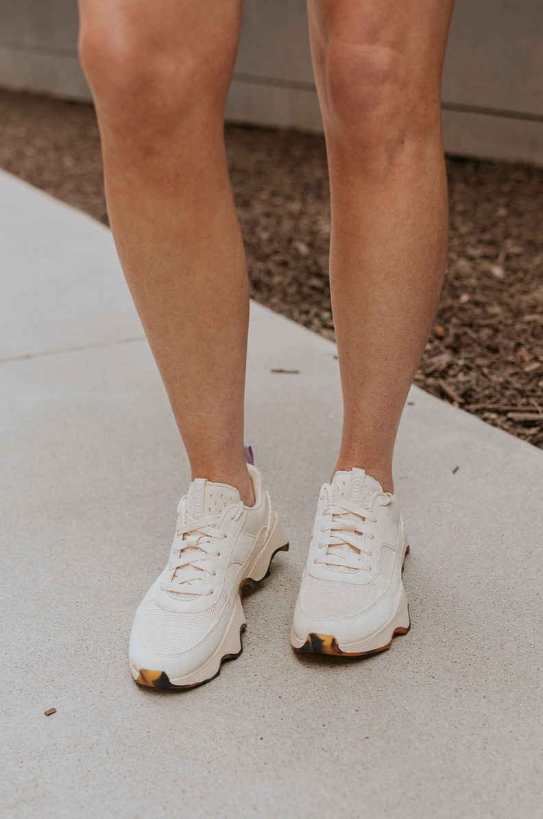 Front view of female model wearing the Kinetic Impact II Wonder Lace Sneaker in Honey White & Euphoric Lilac which features Light Beige Mesh Fabric & Suede/Leather Upper, Tortoise Detail Rubber Sole, Lace Up Details and Lavender Pull Tab .