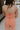 Upper body back view of brunette model wearing the Regan Wide Leg Denim Jumpsuit in Coral, that has coral denim fabric, wide legs, and thin straps.