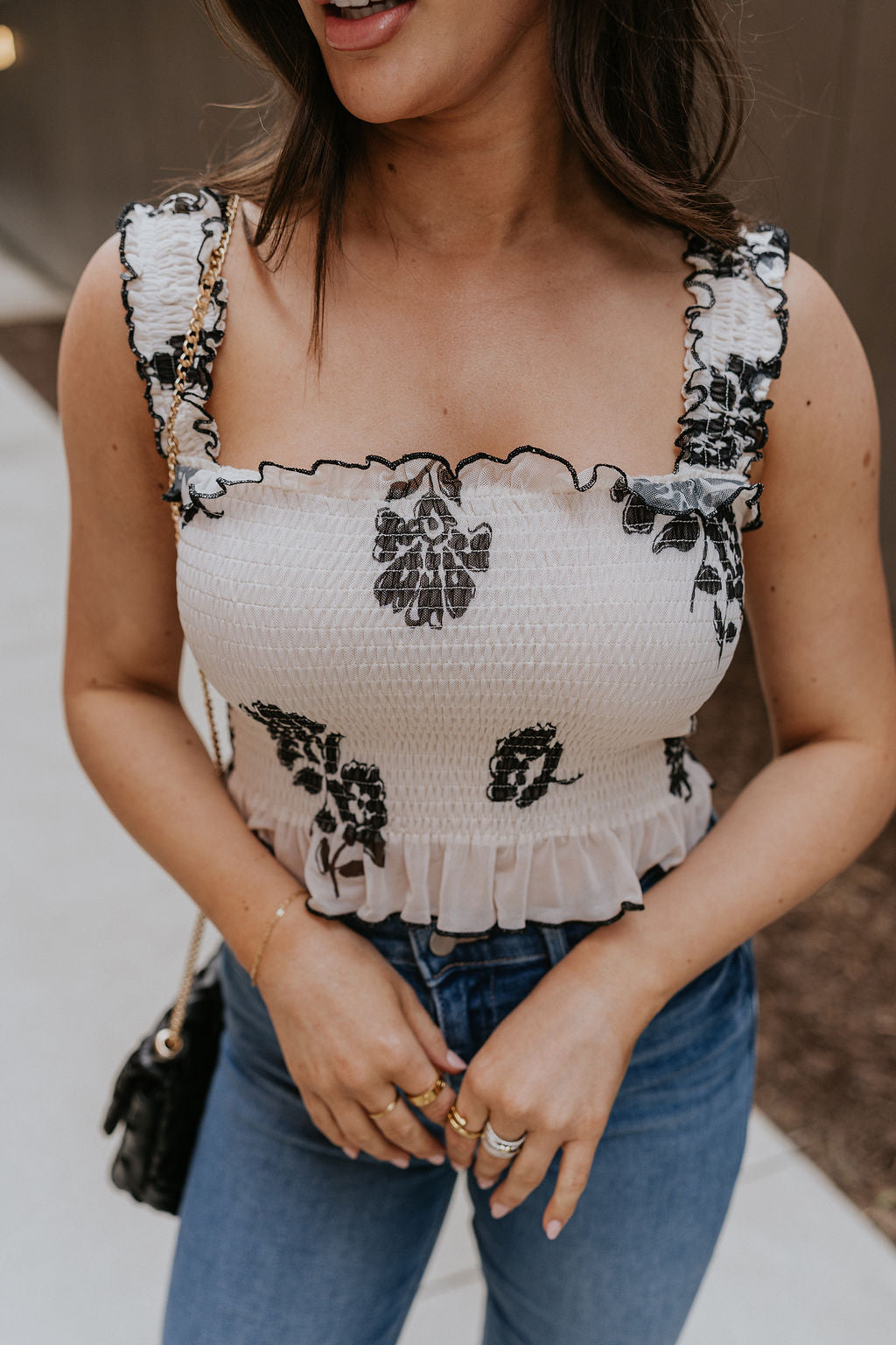 Close up view of female model wearing the Elaina Black & Cream Floral Tank which features Black and Cream Floral Smocked Fabric, Cropped Waist, Lettuce Hem Details, Square Neckline and Thick Straps