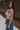 Side view of female model wearing the Elaina Black & Cream Floral Tank which features Black and Cream Floral Smocked Fabric, Cropped Waist, Lettuce Hem Details, Square Neckline and Thick Straps